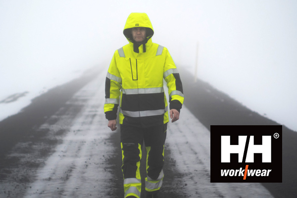 Eine Person, gekleidet in Hi Vis Bekleidung von Helly Hansen, geht durch eine nebelige Schneelandschaft.